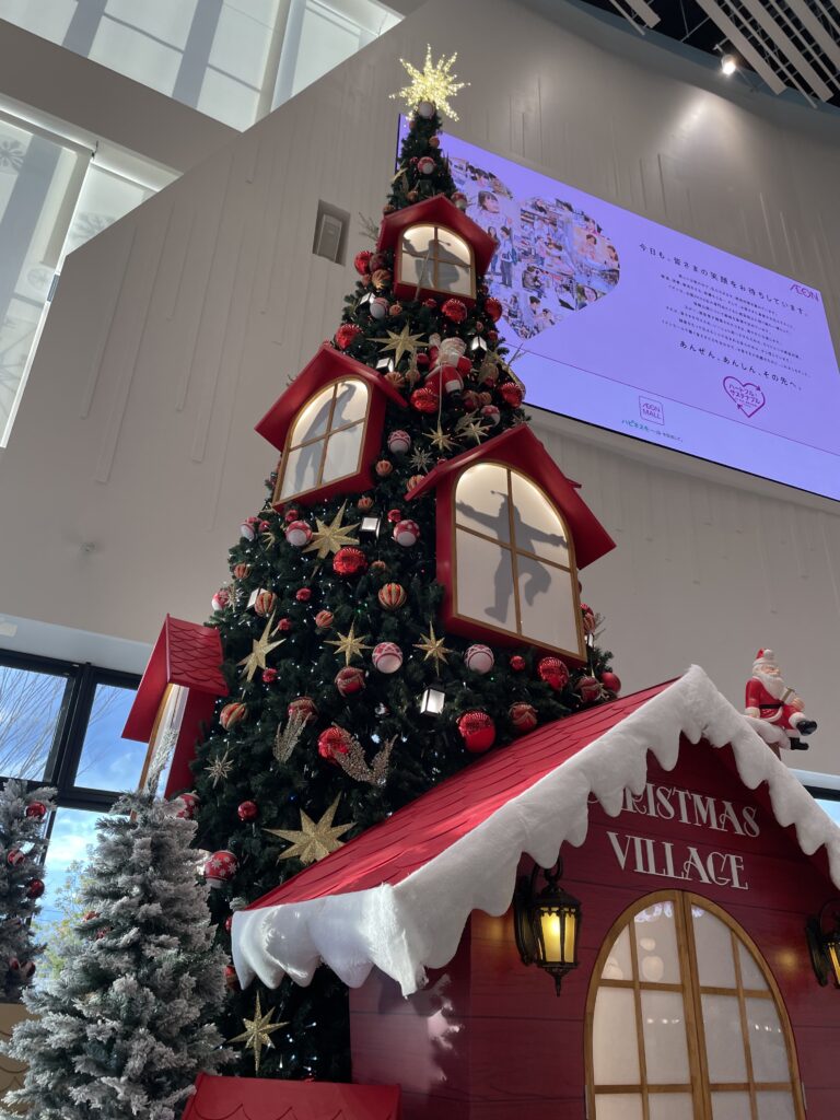 A grand Christmas tree display in a shopping mall, decorated with red and gold ornaments and topped with a glowing star.