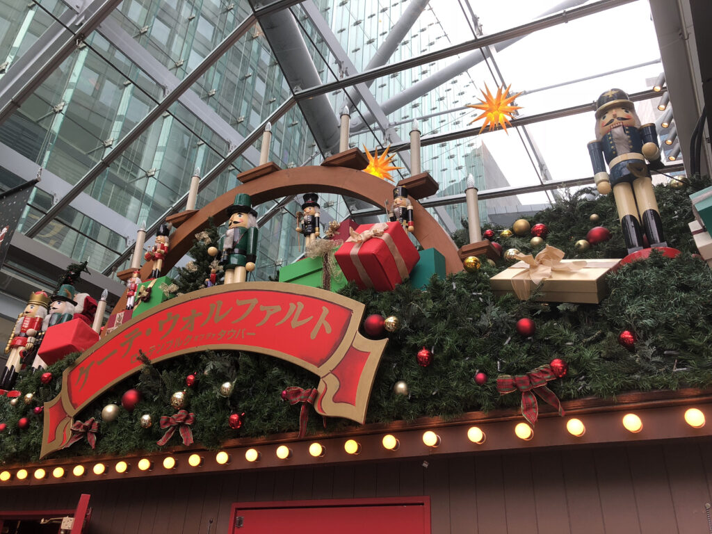 A Christmas market display featuring Nutcracker soldiers, wrapped gift boxes, and festive greenery under a modern glass roof.