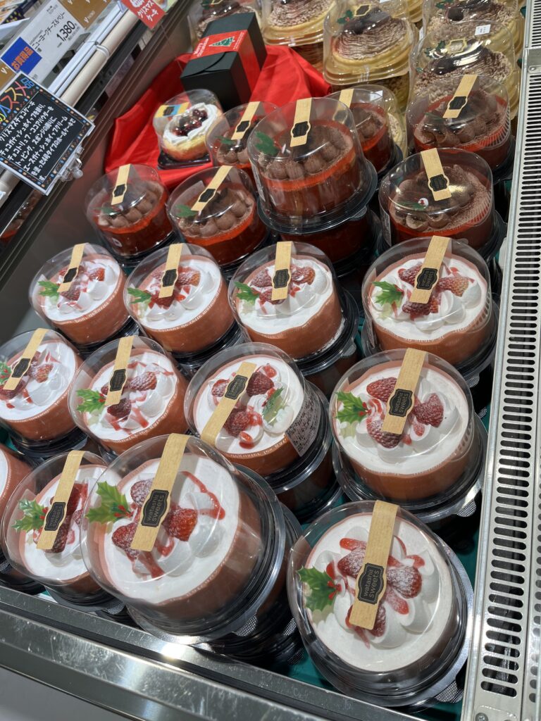 Rows of beautifully decorated Christmas cakes in a store display, topped with strawberries and whipped cream.