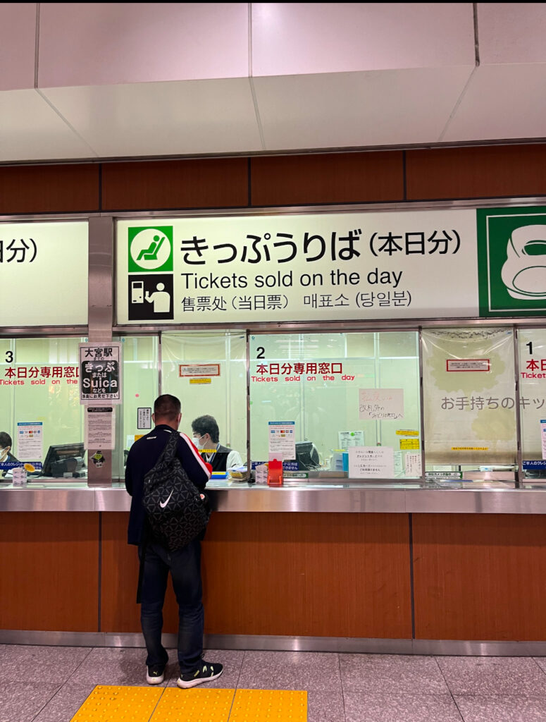 A ticket counter with a sign reading “Tickets sold on the day” in both Japanese and English, with a traveler purchasing a ticket.