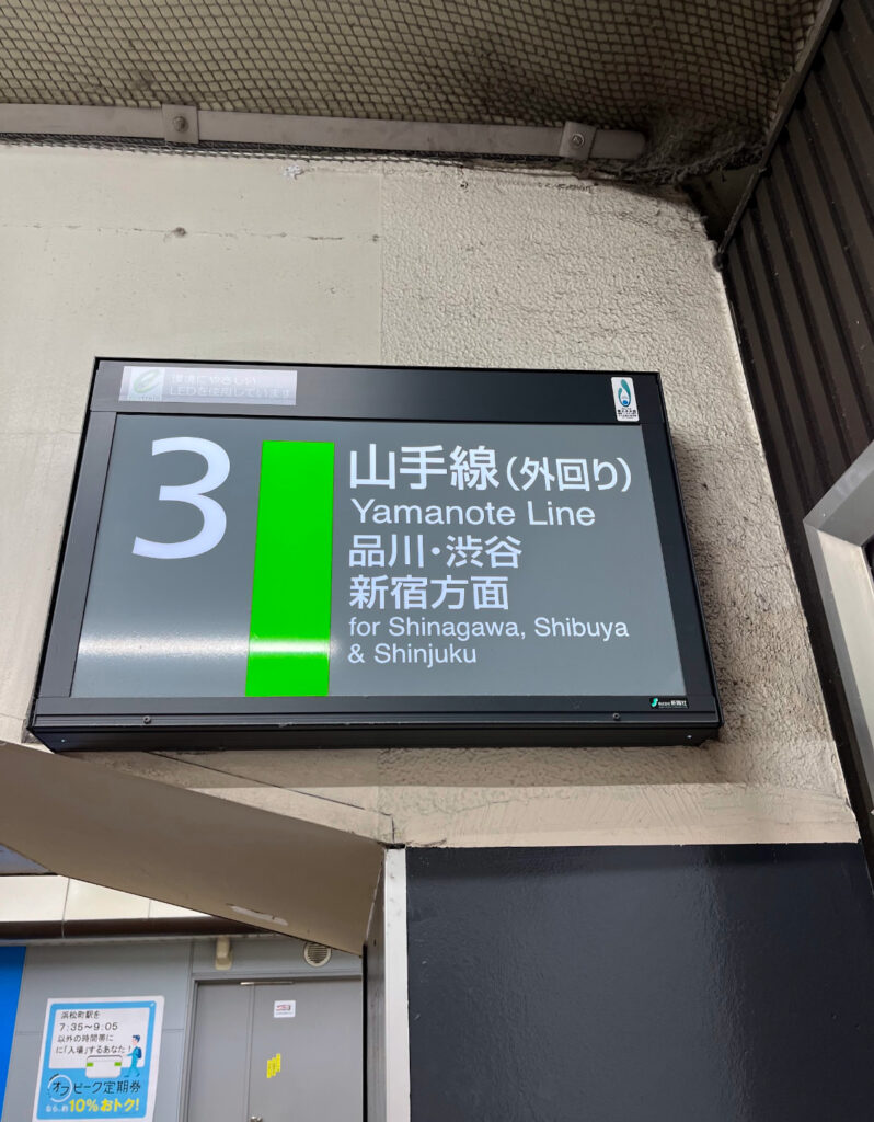 A Yamanote Line platform sign at a Tokyo station, directing passengers to destinations like Shinjuku, Shibuya, and Shinagawa.