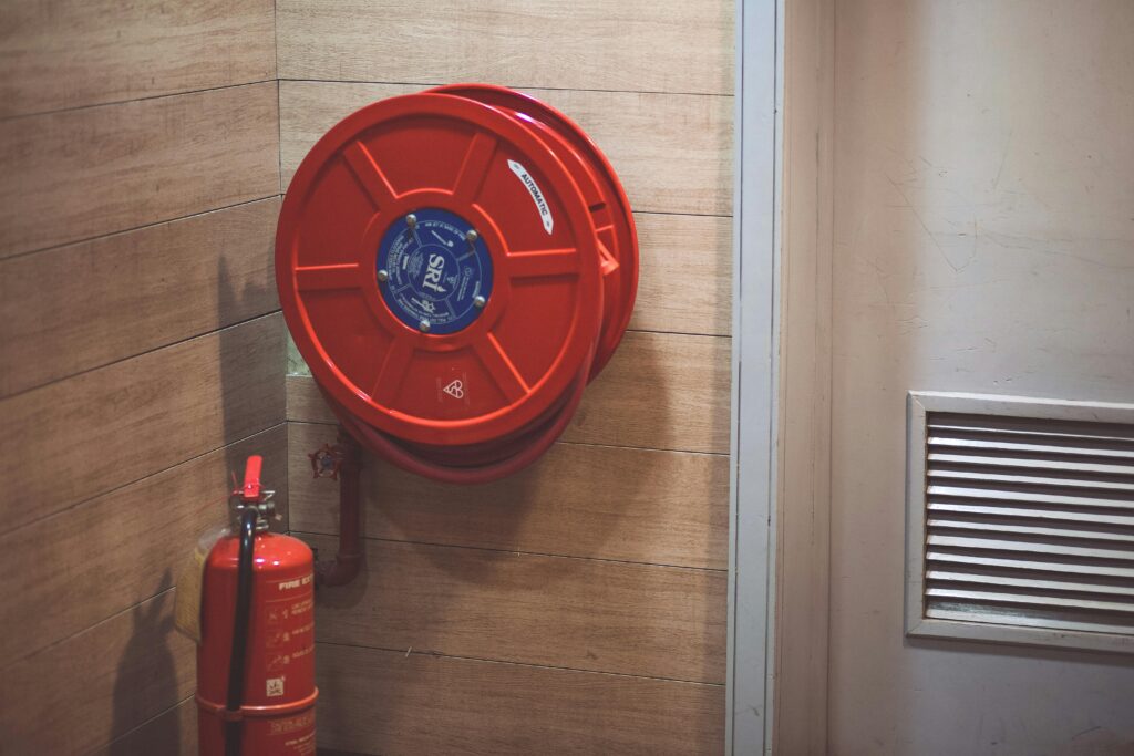 A bright red fire extinguisher and hose mounted on a wooden wall inside an apartment building.