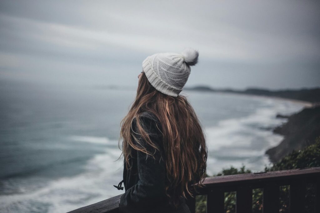 A woman in a white hat looking out over a quiet, misty ocean view.