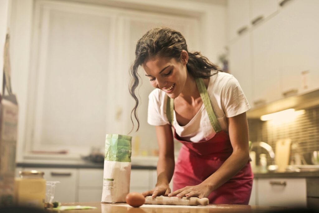 A woman happily rolling dough in a bright kitchen.