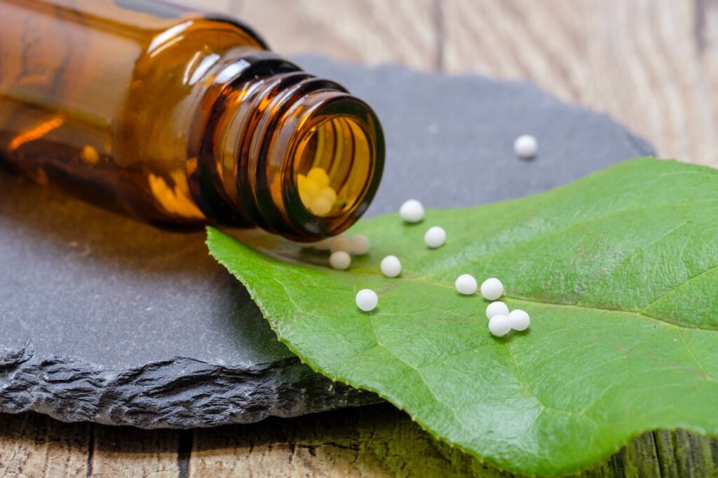 Amber glass bottle with small white pellets spilling onto a green leaf, placed on a slate surface.