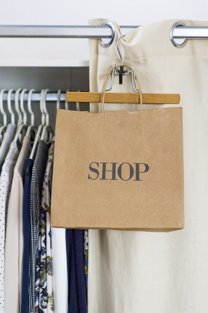 A brown shopping bag with the word 'SHOP' printed on it, hanging on a hanger in a wardrobe filled with neatly organized clothes.