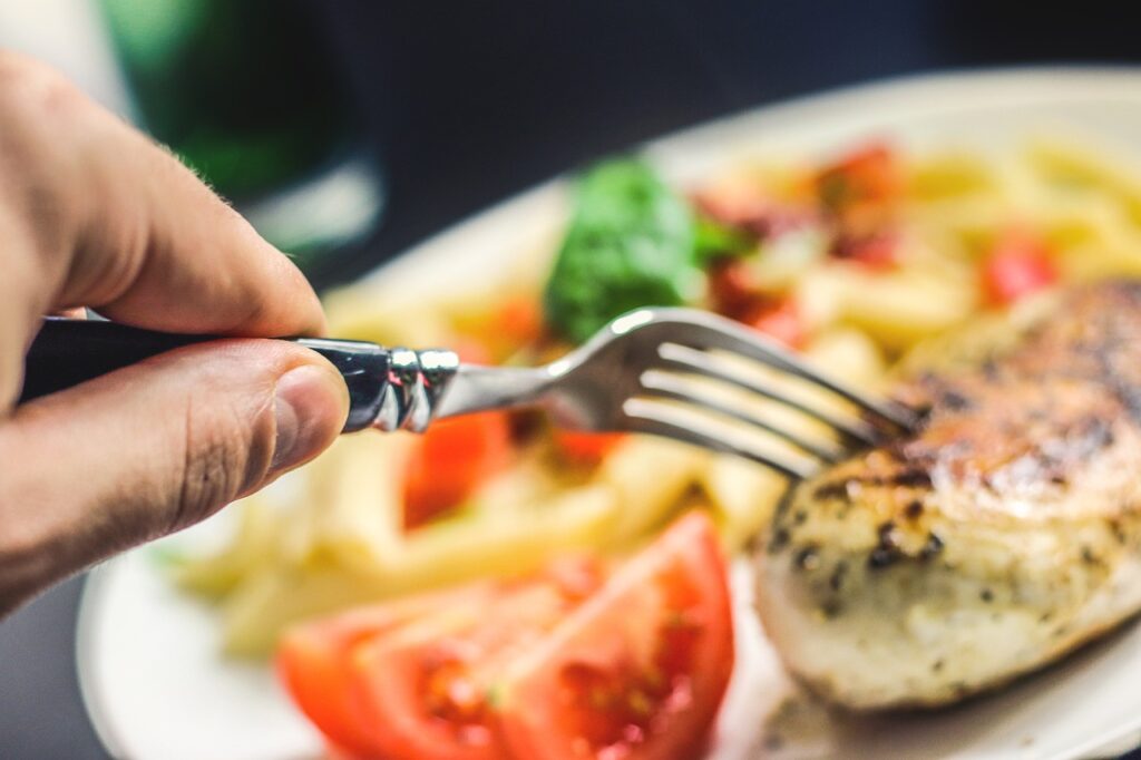 A person holding a fork, about to take a bite of a delicious meal consisting of chicken, tomatoes, and fries.