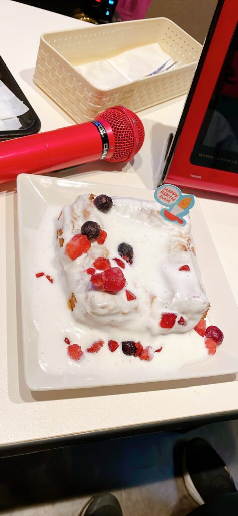  A warm Danish pastry covered in cream and mixed berries on a plate, next to a red microphone inside a karaoke room.