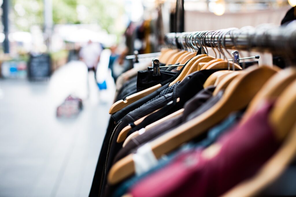 A rack of clothing on hangers displayed in an open-air market, with blurred shoppers in the background.