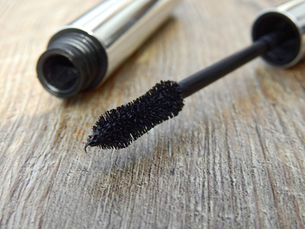  A close-up of a black mascara wand against a wooden surface, emphasizing lash-enhancing beauty trends.