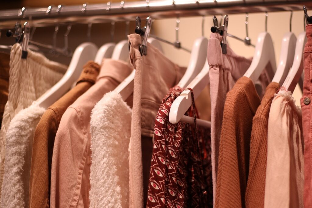 A close-up of a clothing rack displaying soft pastel and earthy-tone formal dress in a cozy boutique.