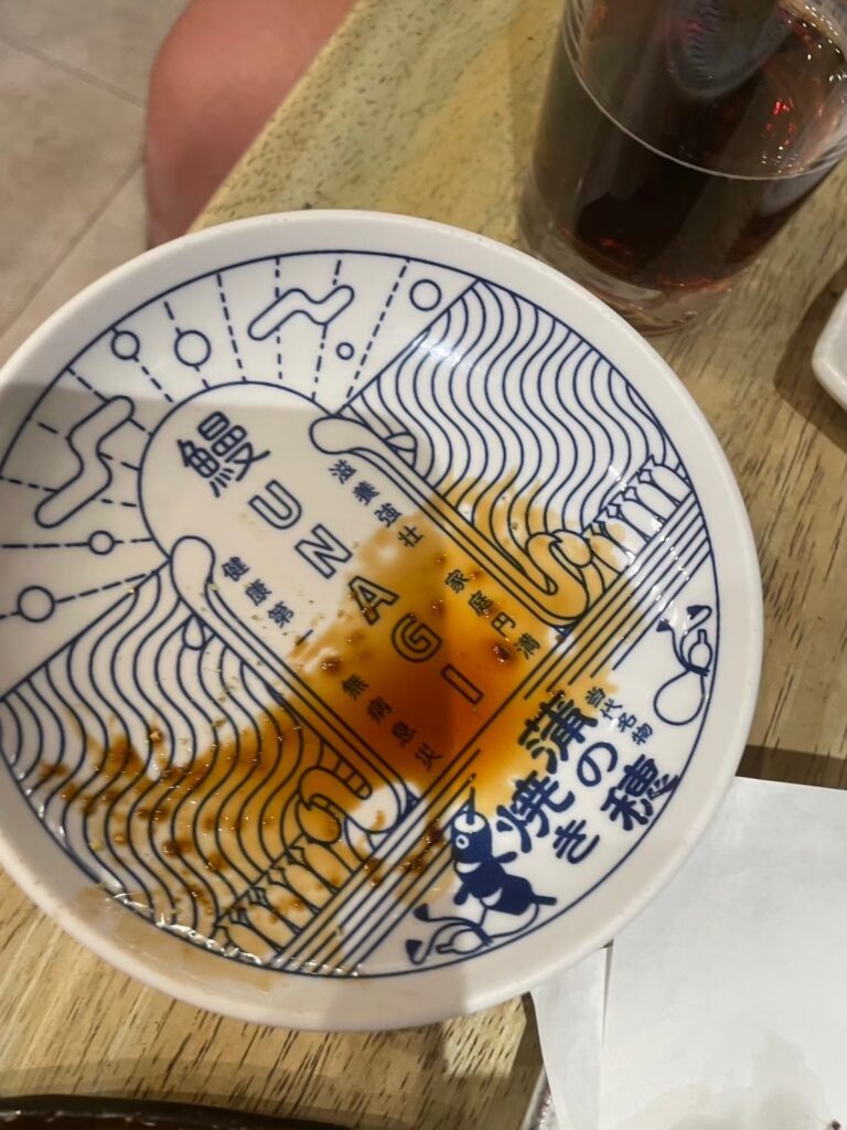 A traditional Japanese bowl with artistic designs and calligraphy at the bottom, showing remnants of eel sauce in Umeda.