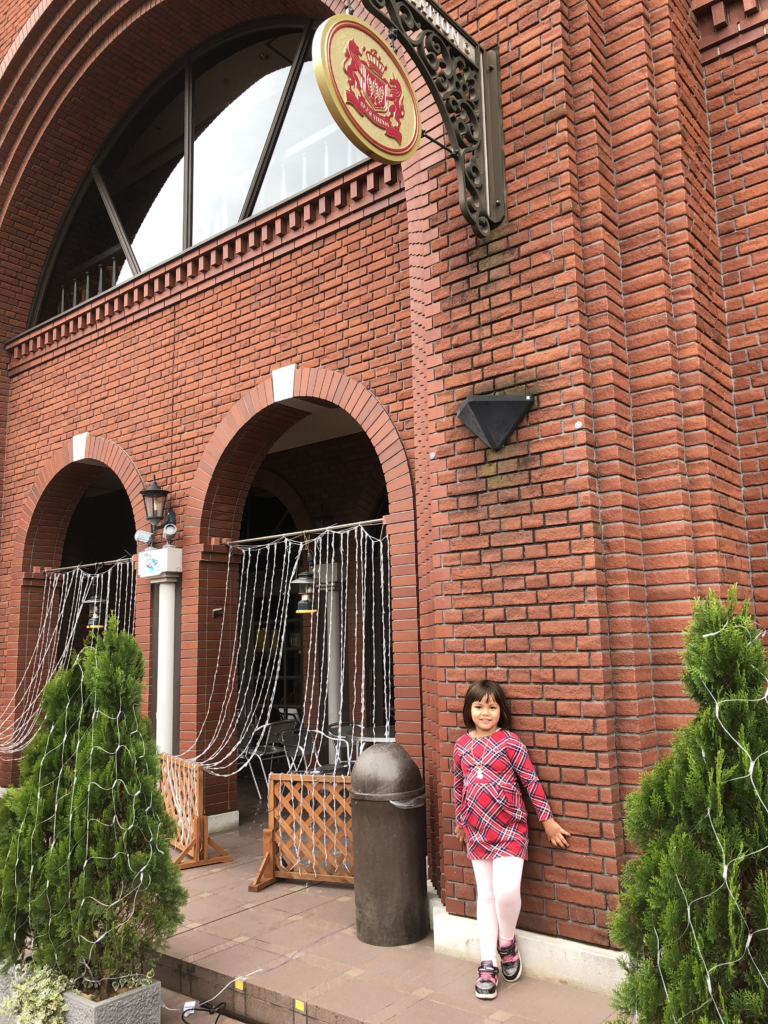  A red brick building in Ebisu Garden Place with a decorative sign and a child posing outside.