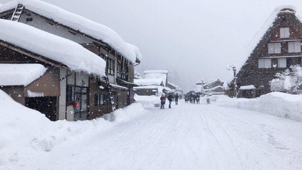 A snow-covered street in Shirakawago with visitors walking and exploring the traditional village during heavy snowfall.