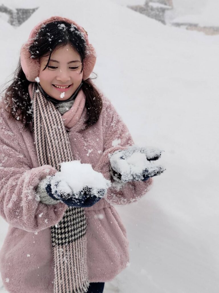 A woman in pink winter attire enjoying freshly fallen snow with a joyful expression.