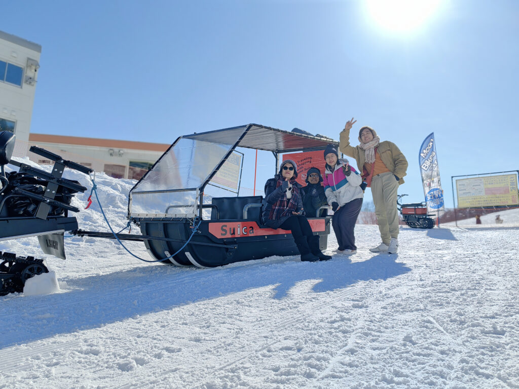 A family posing for a photo on a snowmobile sleigh under a clear blue sky.Caption: Not into skiing? Try the Snowmobile Sleigh Tour for a fun and scenic winter experience.