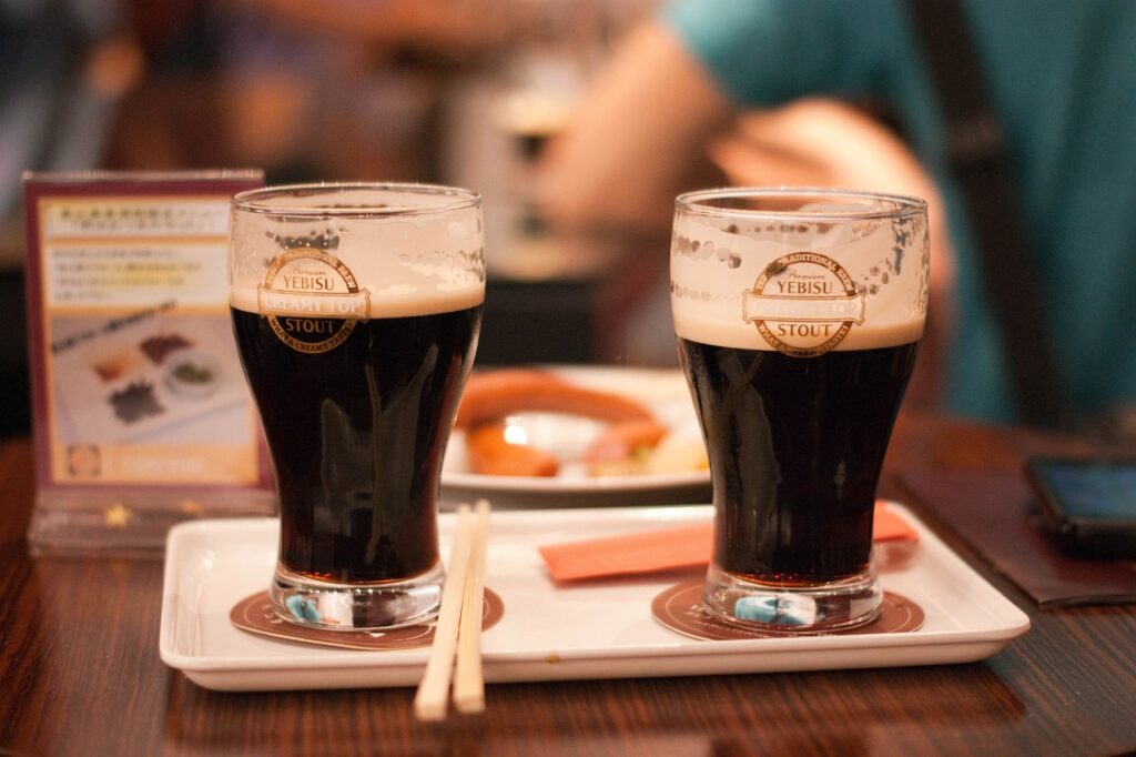  Two glasses of Yebisu Stout beer served on a tray with chopsticks, placed on a wooden table in a restaurant setting.