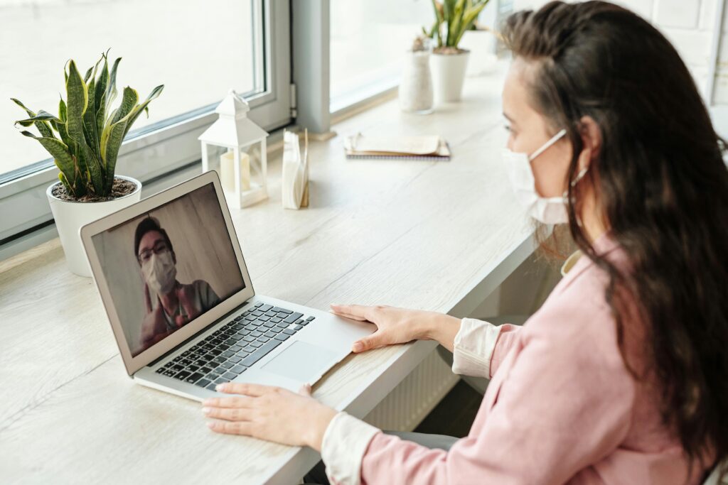 A woman wearing a mask having a virtual consultation on her laptop.