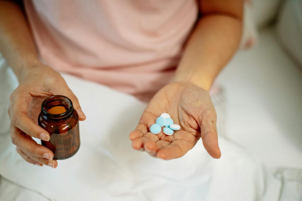 A person holding blue pills in one hand and a brown bottle in the other.