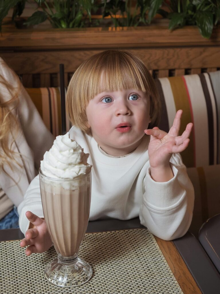 A young child enjoying a milkshake at a café, looking curious and excited. Dining with kids in Japan can be fun with kid-friendly options available in many restaurants.