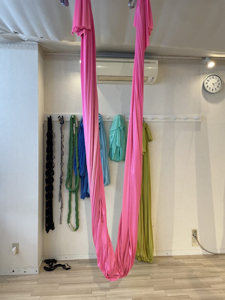 Bright pink aerial yoga silk ropes hanging in an airy studio with various colorful silks in the background.