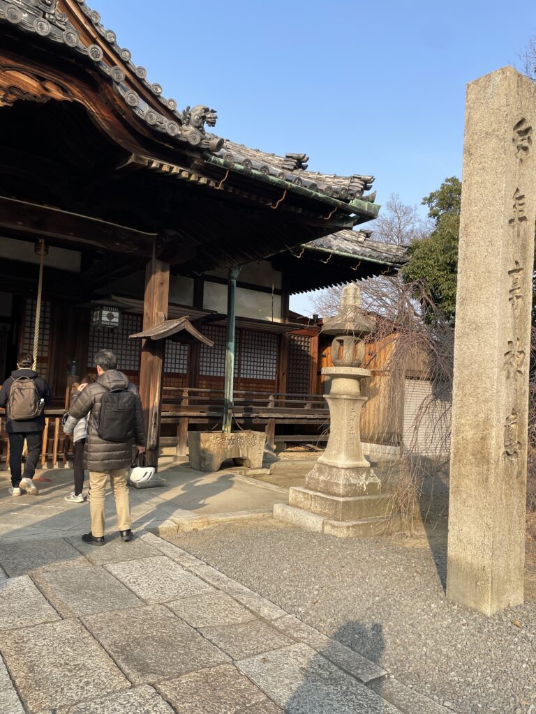 The entrance of Jozenji Temple with a traditional wooden structure, a stone pillar with Japanese inscriptions, and visitors walking inside.