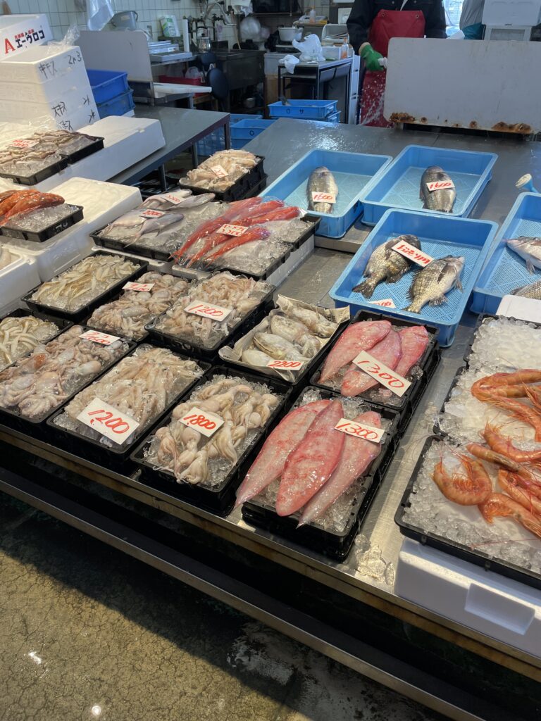 A fresh seafood market stall at Izumisano Fisheries Cooperative Aozora Market, showcasing fish, squid, and shrimp on ice.