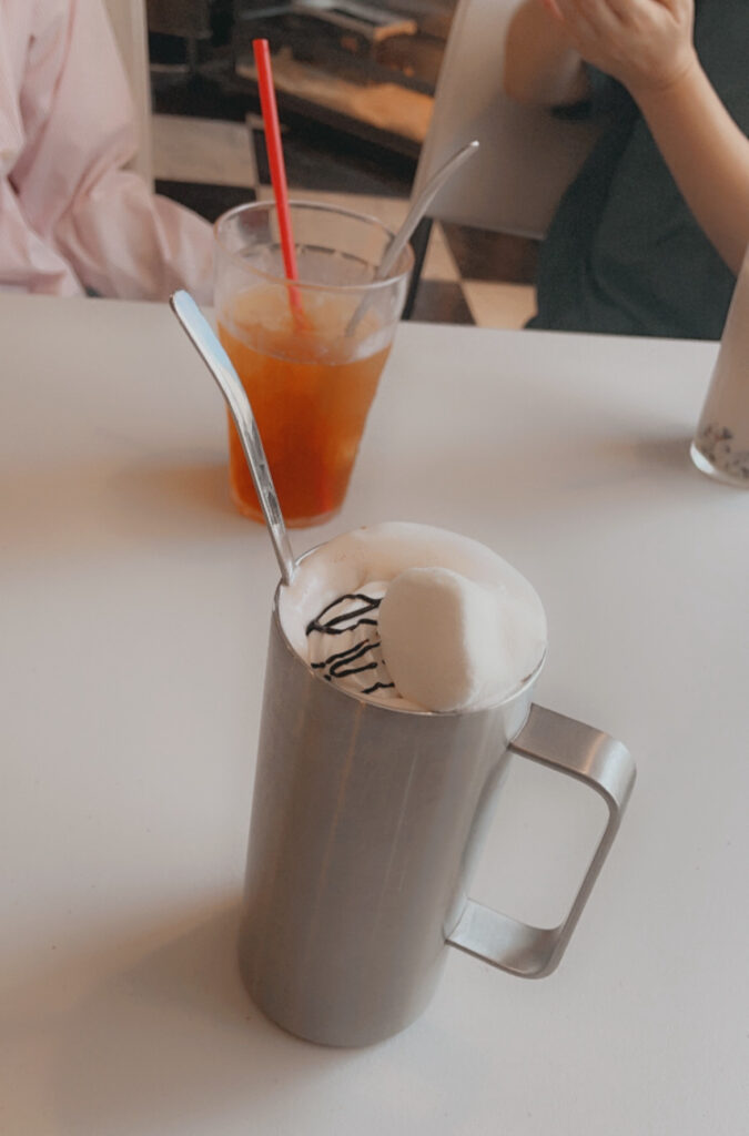 A warm drink topped with whipped cream and chocolate syrup served in a metal mug at ROCKSTAR Café.