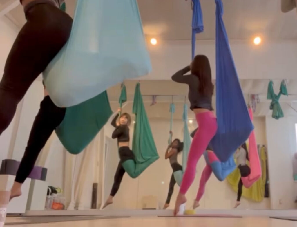  Group of aerial yoga students suspended in colorful silks, stretching and balancing mid-air.