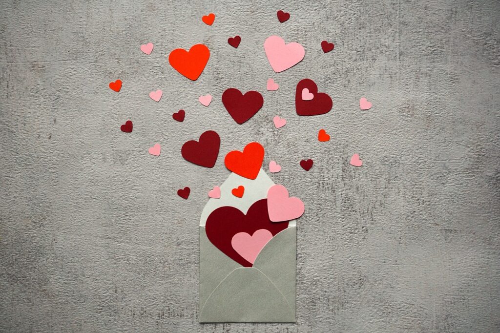 A gray envelope bursts open with red and pink paper hearts, symbolizing love letters and heartfelt emotions.