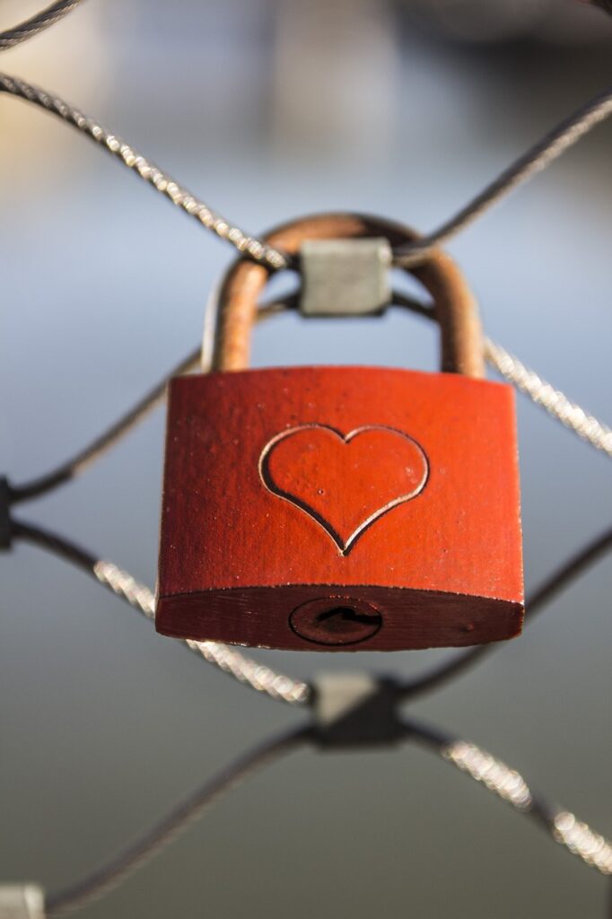 A red padlock with a heart engraving is fastened to a fence, symbolizing everlasting love and commitment.