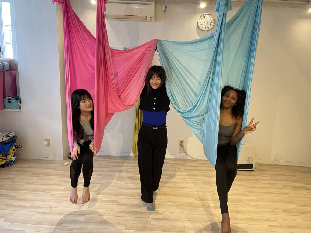 Two friends smiling and posing gracefully with colorful silk ropes, enjoying their aerial yoga experience.