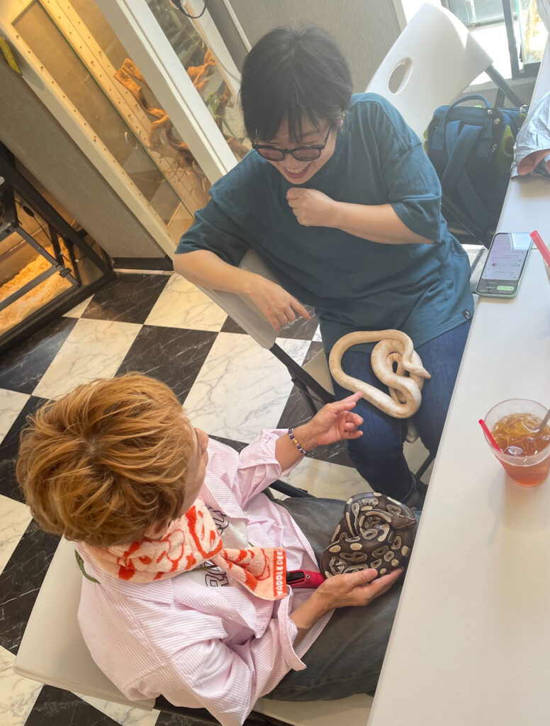 Two friends laughing and chatting while holding different snakes comfortably seated at ROCKSTAR Café.