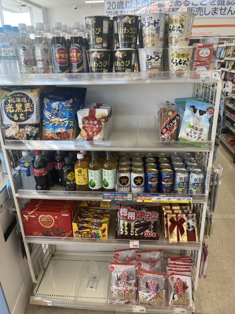  A shelf inside a Seicomart convenience store displaying various Hokkaido specialty products, including wasabi-flavored cup noodles, Hokkaido potato chips, and locally produced snacks and beverages.