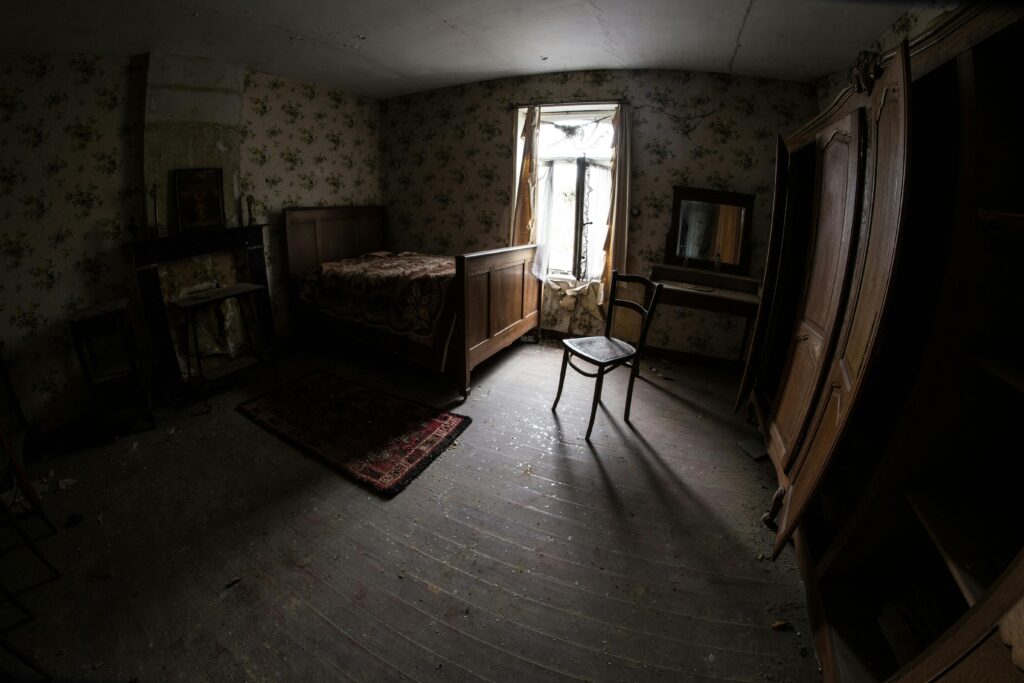 A dark, abandoned bedroom with broken furniture and peeling wallpaper, highlighting signs of poor apartment maintenance.