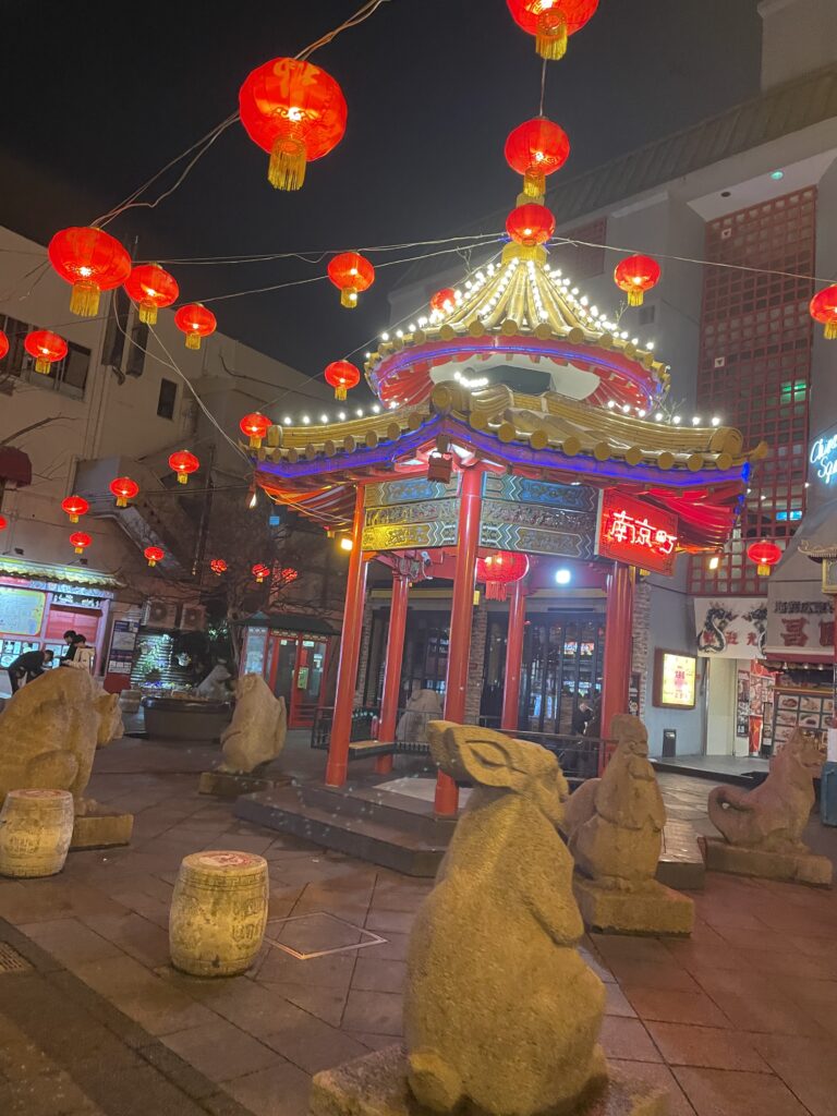 Night view of Kobe Chinatown lanterns and zodiac animal statues surrounding a traditional Chinese pavilion.