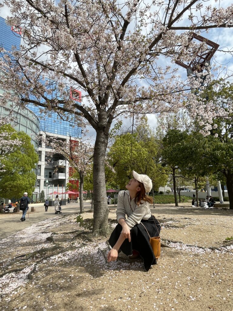 A young woman sitting under a pink tree, admiring the flowers.