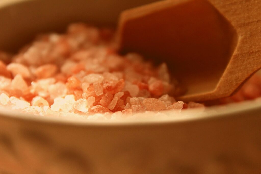 Close-up of pink Himalayan bath salts with a wooden scoop.