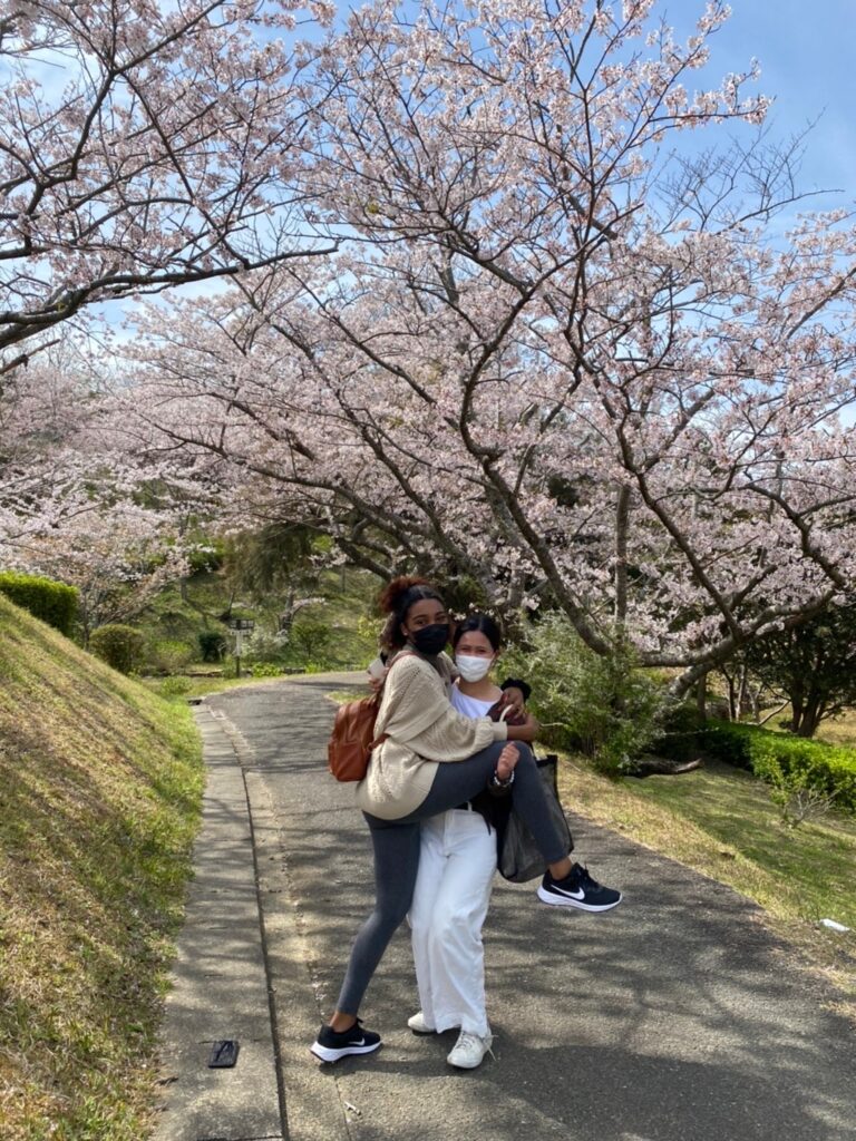 Two friends posing under a row of Sakura trees in full bloom.