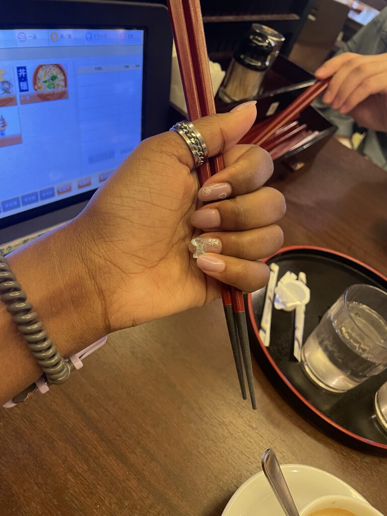  Close-up of a hand holding chopsticks in a restaurant with a touch panel menu in the background