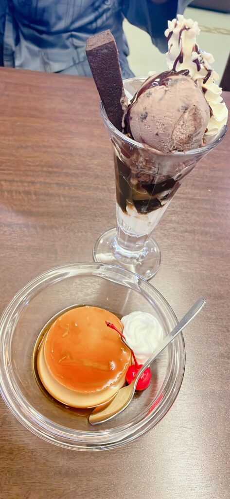 Chocolate parfait with whipped cream and a bowl of flan with cherry and whipped cream on the side