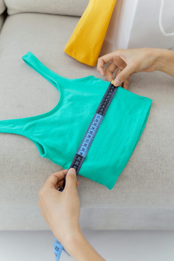 A person measuring a small green tank top with a measuring tape.