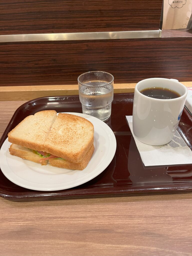 A fruit sandwich, yogurt, and coffee on a café tray.