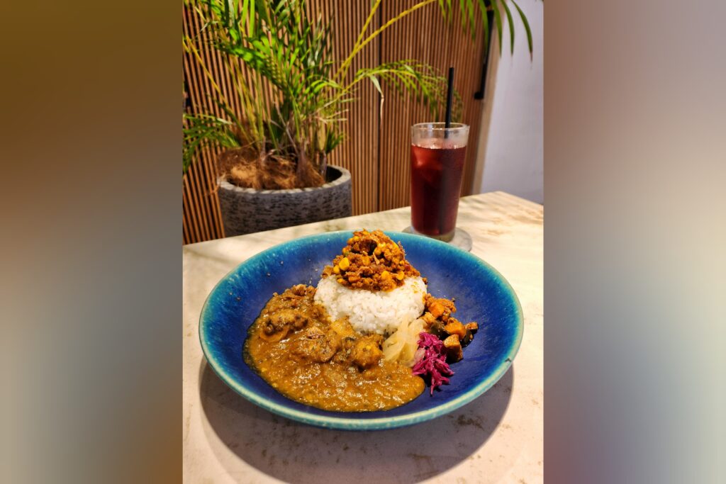 A vibrant plate of curry with rice, topped with minced meat, and served with pickled vegetables and a refreshing cranberry juice.