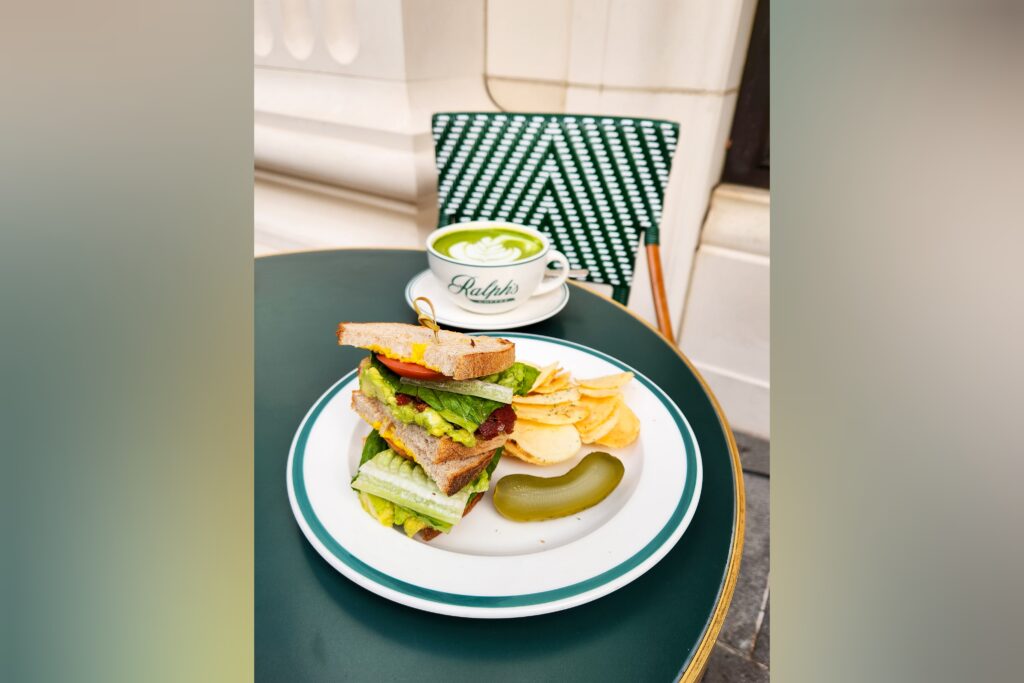 A plate with a BLAT (bacon, lettuce, avocado, and tomato) sandwich, served with potato chips and pickles.