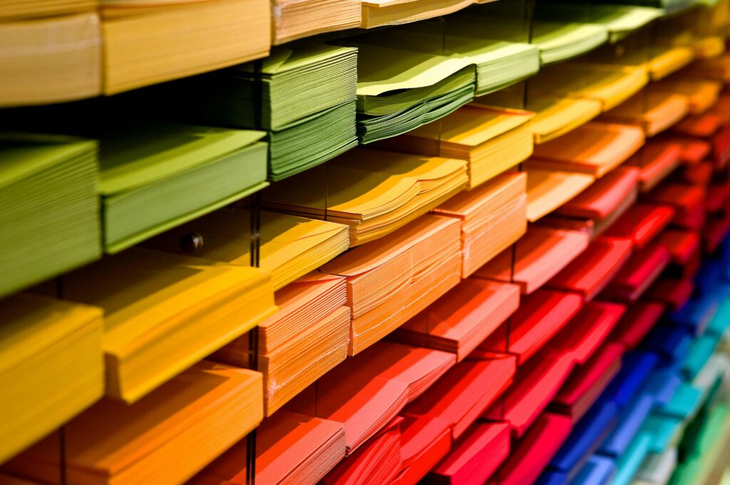 A neatly organized stack of multicolored paper arranged on shelves, featuring vibrant shades of green, yellow, orange, and red.