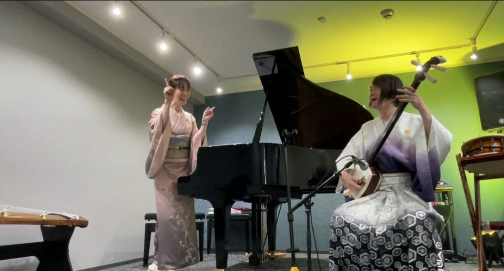 Two women in kimono performing with traditional Japanese instruments and a piano.