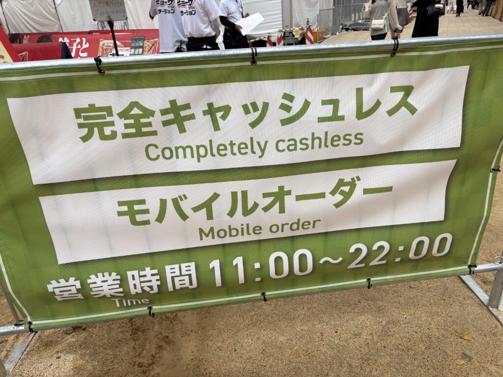 Green sign at the Osaka food expo stating the event is cashless and supports mobile orders.