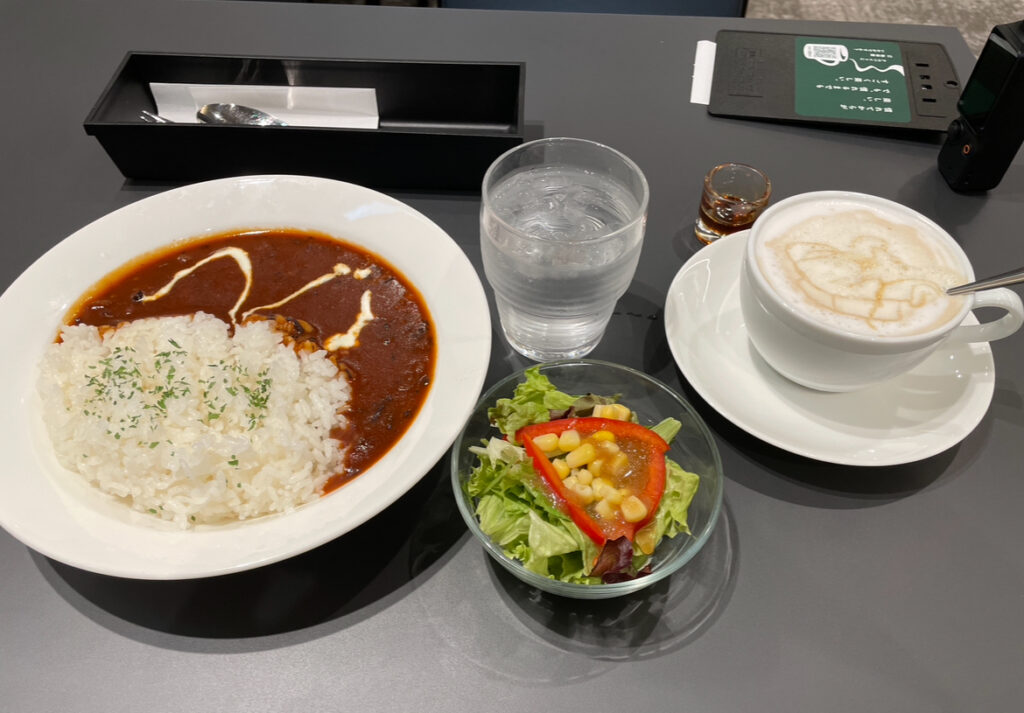 A hearty meal of curry rice, salad, and a cappuccino set on a modern café table