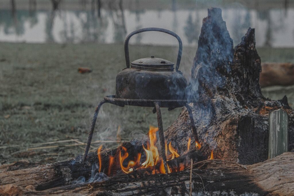 Old kettle heating over a campfire beside a log in the forest.